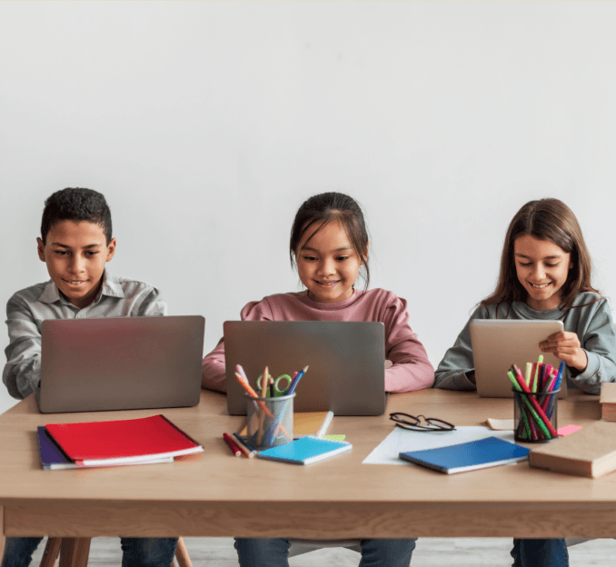 happy children sitting at a table with laptops open, illustrating the idea behind mindeasy, an edtech & neurotechnology startup case study by mobitouch