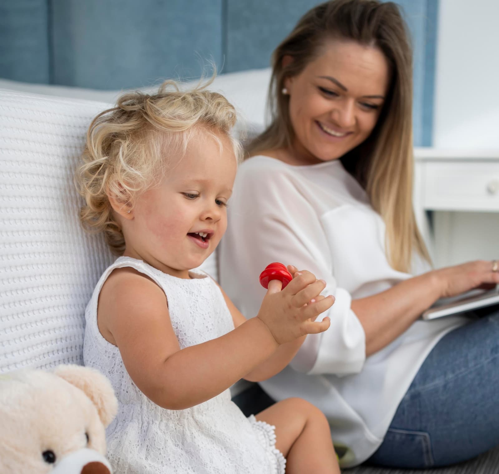 Mom with a laptop on her lap smiling at her little daughter playing with a red toy