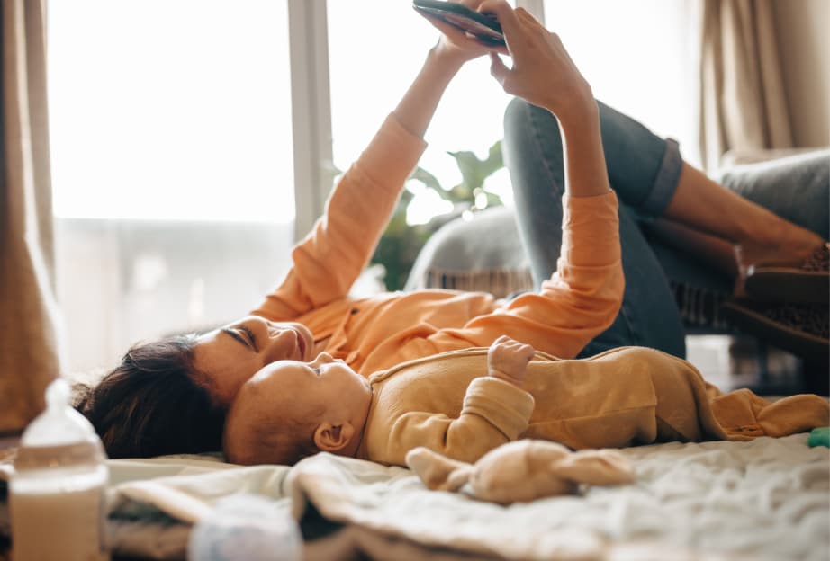 Mom lying on a blanket with her baby, holding a smartphone above them