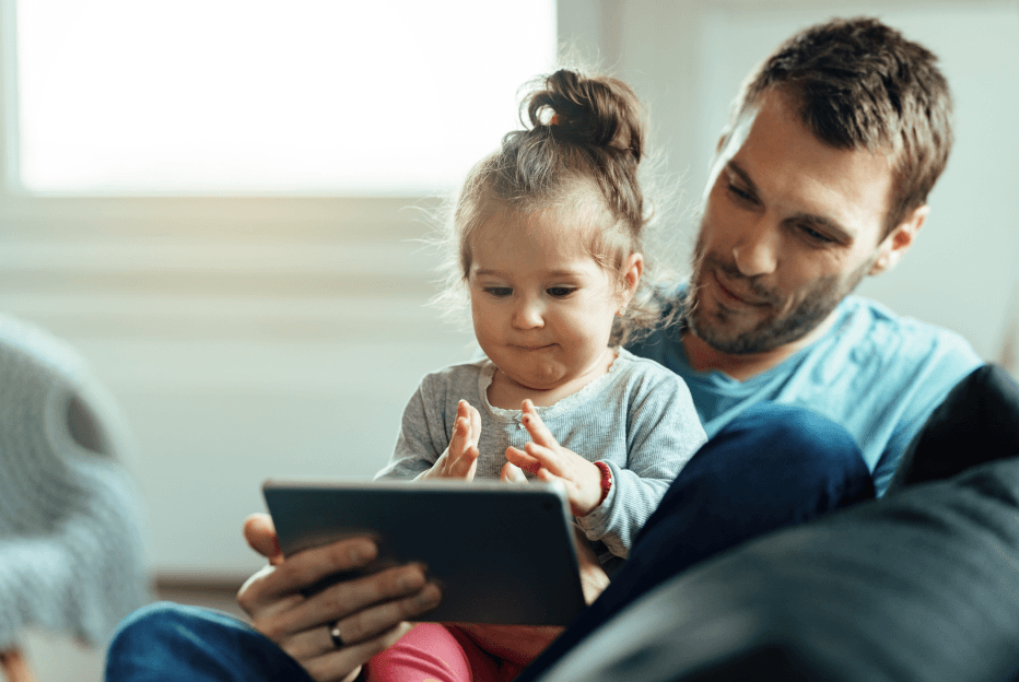 Tata z małą córką na kolanach korzysta z tabletu w domu